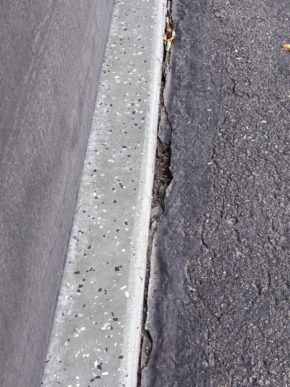 Cracked asphalt along a concrete gutter edge