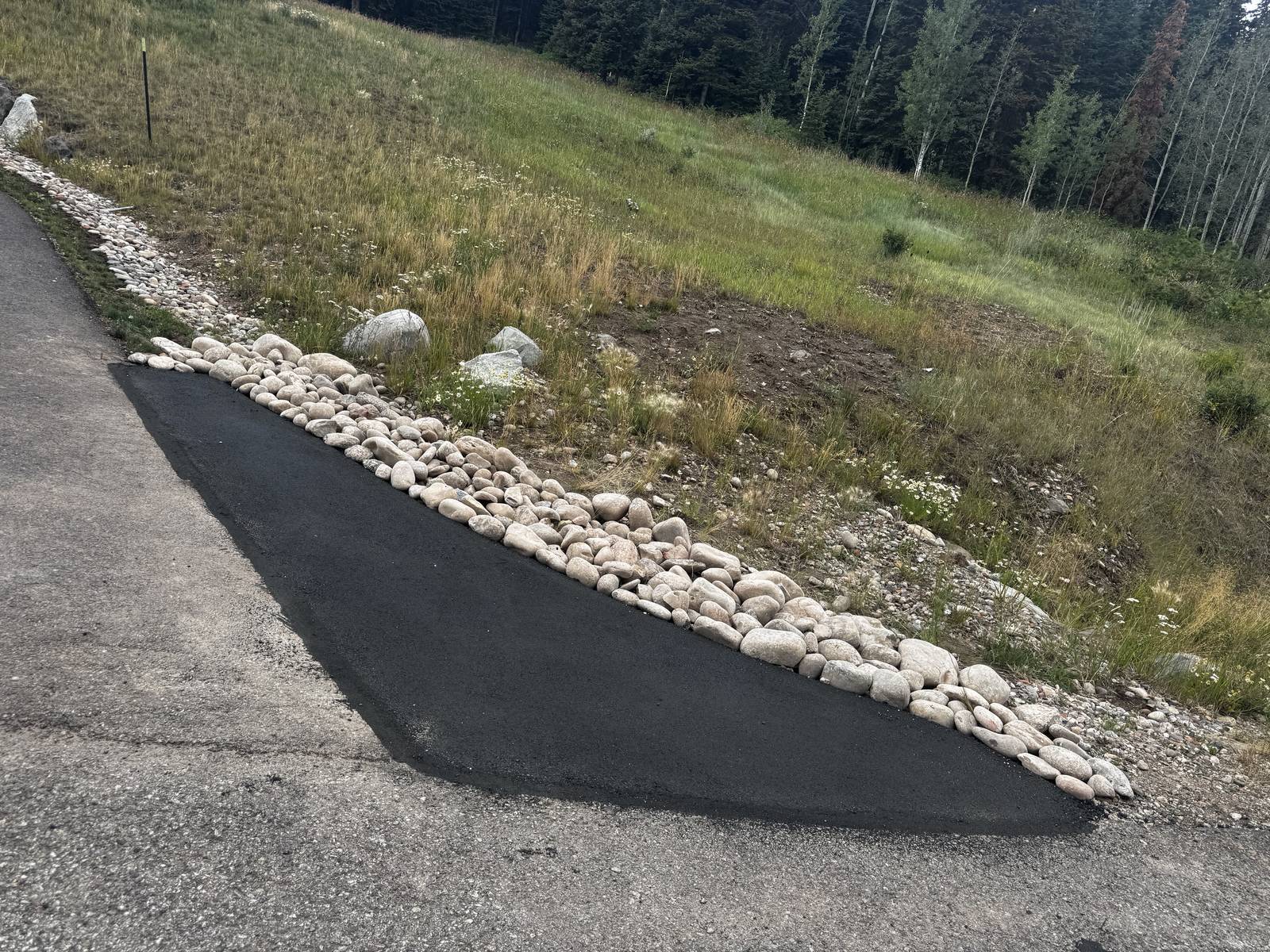 A fresh strip of asphalt laid tight against a river rock border on a mountain driveway