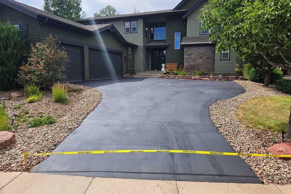 A freshly sealcoated driveway curving up to the garage, caution tape still across the apron